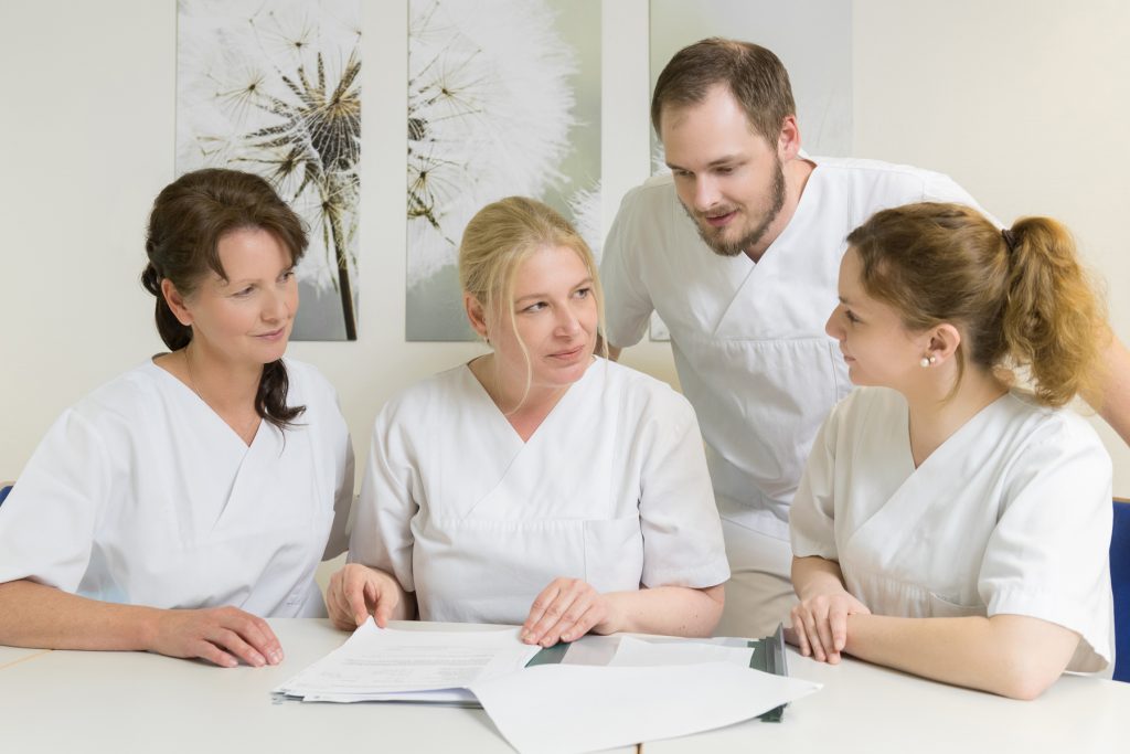 Vier Pflegekräfte besprechen im Sitzen eine Patientenakte.
