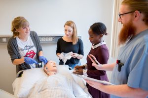 Ein Pfleger erklärt drei Schülerinnen wie sie einen Patienten richtig versorgen